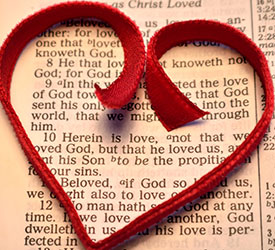 Image of a red ribbon shaped into a heart laying on top of a bible verse