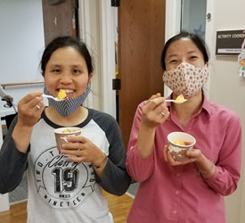 Sisters Nga Tran and Hong Bui enjoying peaches during a farmers market event at Our Lady of Good Counsel, Mankato, Minnesota. 