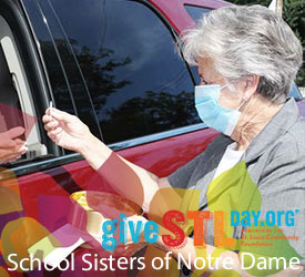 Sister Janice Munier hands out communion to a parishioner in their car in St. Louis. The image contains the Give STL Day logo, School Sisters of Notre Dame and boardered by Jubilee 2021 logo image. 
