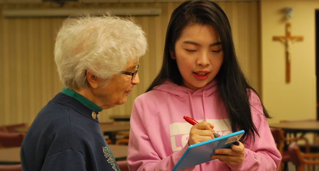 A photo with Sister Sister Gina Redig and Sin Leng Lei discuss art through writing on a dry erase board while at Notre Dame Elm Grove, Elm Grove, Wisconsin. 