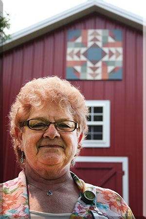 Ellen Graham in front of barn quilt on Our Lady of Good Counsel campus