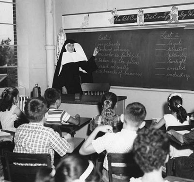 A historical black and white photo of a School Sister of Notre Dame teaching students at Catholic Central High School. 