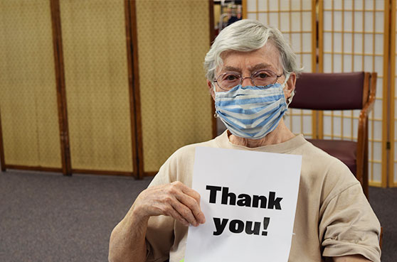 Sister recieves her COVID-19 vaccine at Notre Dame of Elm Grove, Elm Grove, Wisconsin. She holds up a thank you sign.